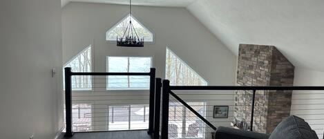 Amplia habitación estilo loft con techo alto, chimenea de piedra y vistas al exterior a través de amplias ventanas.