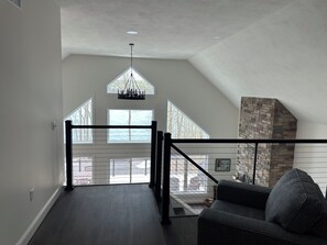 Amplia habitación estilo loft con techo alto, chimenea de piedra y vistas al exterior a través de amplias ventanas.