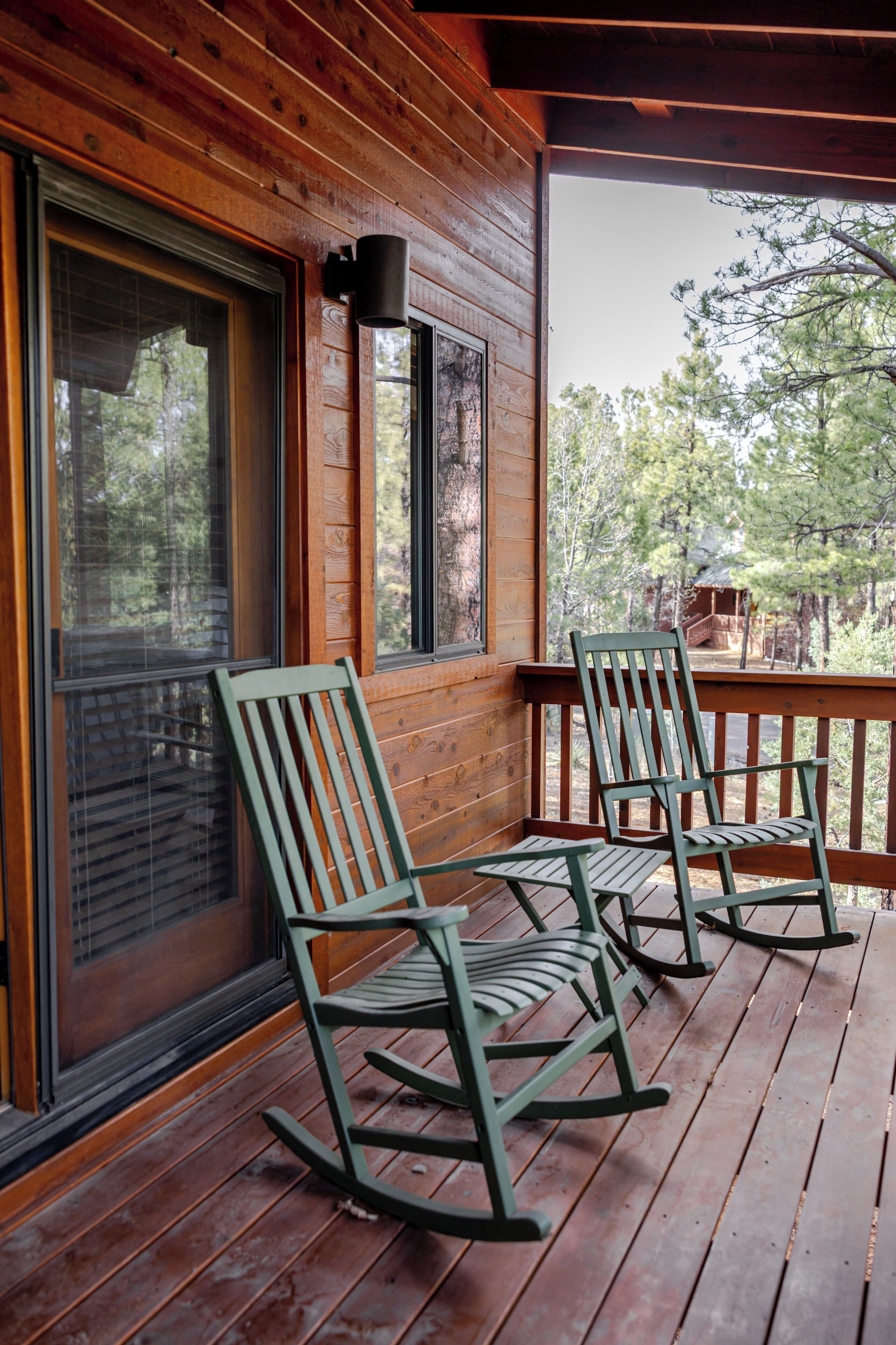 A wooden porch with two rocking chairs and a window overlooking a forest.