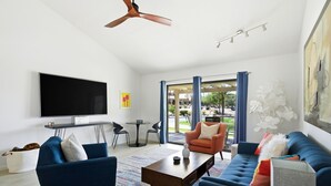 A modern living room with a flat-screen TV, two sofas, a coffee table, and a ceiling fan. - 10th Tee Retreat - Mountain Views + Resort Living (Palm Desert)