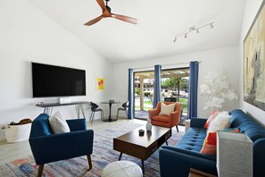 A modern living room with a flat-screen TV, two sofas, a coffee table, and a ceiling fan. - 10th Tee Retreat - Mountain Views + Resort Living (Palm Desert)