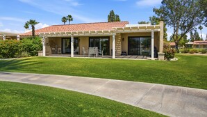 A modern house with a covered patio, a lawn, and a clear blue sky. - 10th Tee Retreat - Mountain Views + Resort Living (Palm Desert)