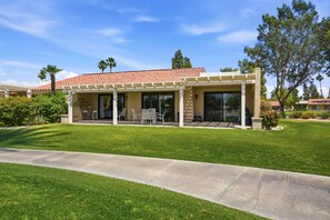 A modern house with a covered patio, a lawn, and a clear blue sky. - 10th Tee Retreat - Mountain Views + Resort Living (Palm Desert)