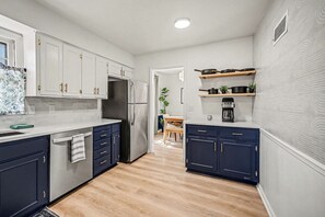 Eine moderne Küche mit weißen und dunkelblauen Schränken, einem Edelstahlkühlschrank und Holzboden.