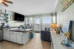 A modern kitchen with a central island, a dining area with a sofa, and a TV mounted on the wall. - Beachfront condo at Seascape w/view from over-sized balcony with w/d in unit (Galveston)