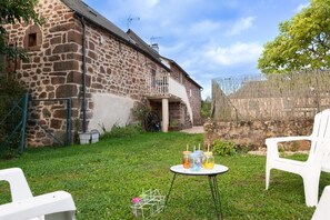 A stone building with a balcony, a grassy yard, and a table with drinks. - Gîte en Grès Rose 4/6 persons (CANILHAC)