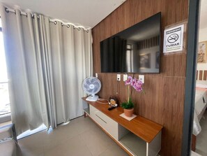 Ein Hotelzimmer mit einer Holzkonsole, einem Flachbildfernseher, einem Ventilator, einer Topf-Orchidee und einem Rauchverbot-Schild.