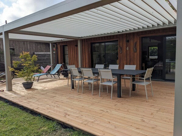 A covered patio with a table and chairs, a potted plant, and a wooden fence in the background. - House near lake and ocean in family resort (Hourtin)