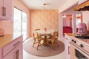 A kitchen with a round dining table, wooden chairs, a pink toaster, and a patterned wallpaper.