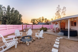 Une terrasse extérieure avec des fauteuils Adirondack blancs, un foyer et un espace équipé d’un bain à remous.