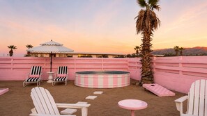 A pink-walled outdoor area with a hot tub, lounge chairs, and a palm tree.