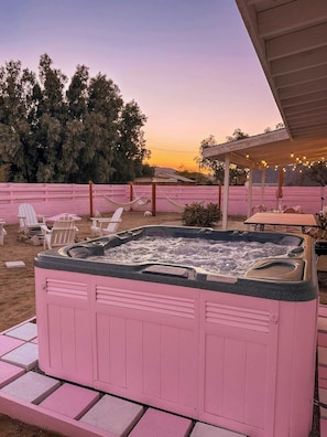 Un jacuzzi rose avec une terrasse en bois, entouré de chaises roses et d’un patio couvert.