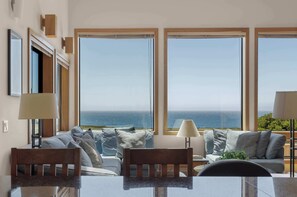 A room with a large window, a sofa, a table, and a lamp. - Stunning Oceanfront Home with 3 Ensuites + Hot Tub (Sea Ranch)