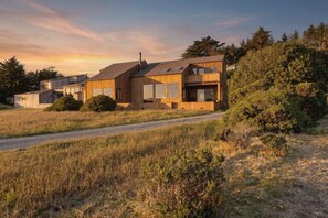 A modern house with a sloped roof, large windows, and a driveway leading to the entrance. - Stunning Oceanfront Home with 3 Ensuites + Hot Tub (Sea Ranch)