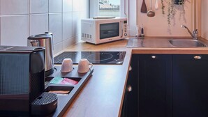 A modern kitchen with a microwave, kettle, and coffee maker on the counter, a built-in oven, and a window with a view of a building. - Le Carrousel - Haussmann hyper-centre Troyes - Quiet and rooftop views (Troyes)