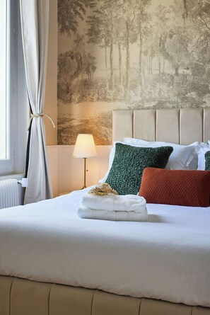 A neatly made bed with a headboard, a lamp, and a wall with a forest mural. - Le Carrousel - Haussmann hyper-centre Troyes - Quiet and rooftop views (Troyes)