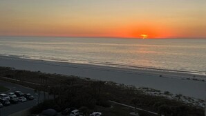 Tramonto sulla spiaggia, con una strada e auto parcheggiate in primo piano.