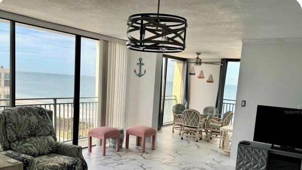 Un soggiorno con una grande finestra, un divano, due sgabelli rosa, una televisione e una poltrona con motivo decorativo.