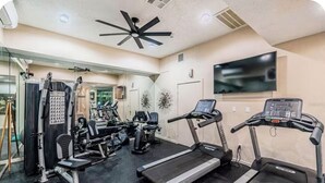 Un gimnasio con cintas de correr, máquinas de pesas y un ventilador de techo.