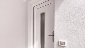 A white door with a frosted glass panel, a door handle, and a light switch on the wall. - Brand new Attic Studio Apartment, air Conditioned (Castelsardo)