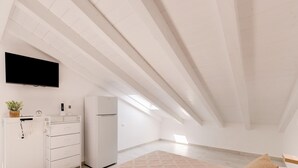 A minimalist room with a bed, a dresser, a refrigerator, and a flat-screen TV mounted on the wall. - Brand new Attic Studio Apartment, air Conditioned (Castelsardo)