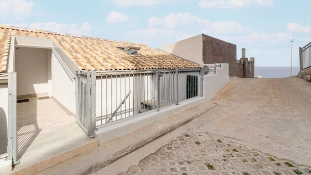 A building with a tiled roof, a metal gate, and a paved area leading to a beach. - Brand new Attic Studio Apartment, air Conditioned (Castelsardo)