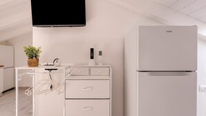 A modern kitchen with a flat-screen TV, a white refrigerator, a white cabinet with drawers, a small plant, and a white hanging rack. - Brand new Attic Studio Apartment, air Conditioned (Castelsardo)