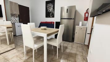 Cocina compacta con mesa, sillas, refrigerador y extintor.