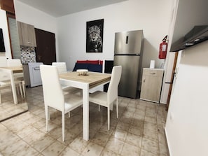 A compact kitchen with a dining table, chairs, a refrigerator, and a fire extinguisher. - baia verde holiday (Baia Verde)
