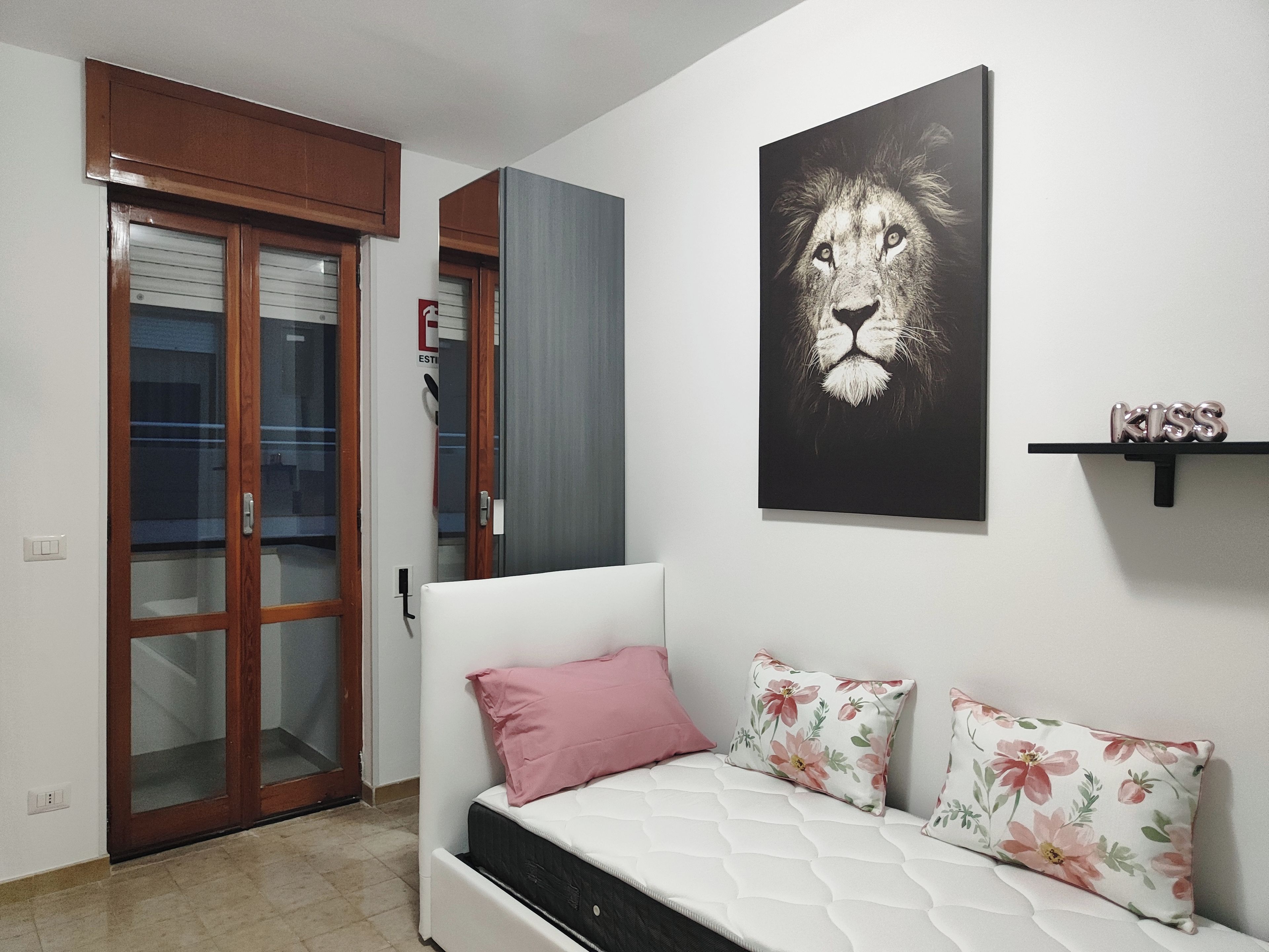 Un dormitorio con cama, una puerta, un cuadro en la pared y una estantería.