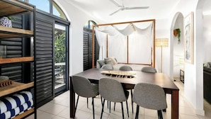A modern dining area with a large table, grey chairs, a ceiling fan, and a view through a glass door. - The Palms at Mango Lagoon—Palm Cove Wellness Haven (Palm Cove)