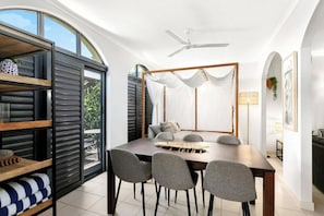 Ein moderner Essbereich mit großem Tisch, grauen Stühlen, Deckenventilator und Blick durch eine Glastür.
