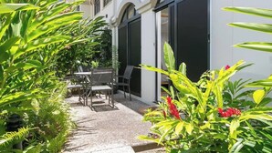 A patio with outdoor furniture, a white building with large windows, and lush greenery. - The Palms at Mango Lagoon—Palm Cove Wellness Haven (Palm Cove)
