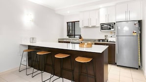 A modern kitchen with a central island, bar stools, a microwave, and a refrigerator. - The Palms at Mango Lagoon—Palm Cove Wellness Haven (Palm Cove)