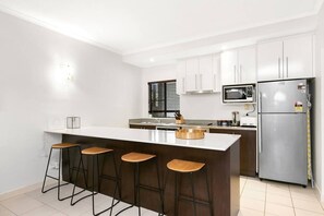 Eine moderne Küche mit einer zentralen Kochinsel, Barhocker, einer Mikrowelle und einem Kühlschrank.