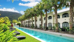 A poolside area with a long pool, palm trees, and a building with arched windows. - The Palms at Mango Lagoon—Palm Cove Wellness Haven (Palm Cove)
