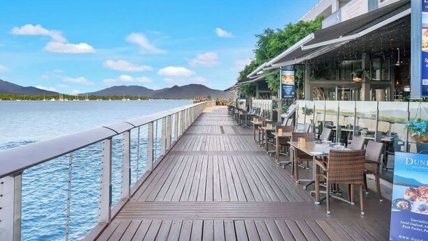 A wooden deck with tables and chairs, overlooking a body of water and mountains. - Waterfront at Harbour Light—Generous Space & Views (Cairns)