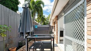 Un espace patio avec une table et des chaises, un parasol et un jardin clos.