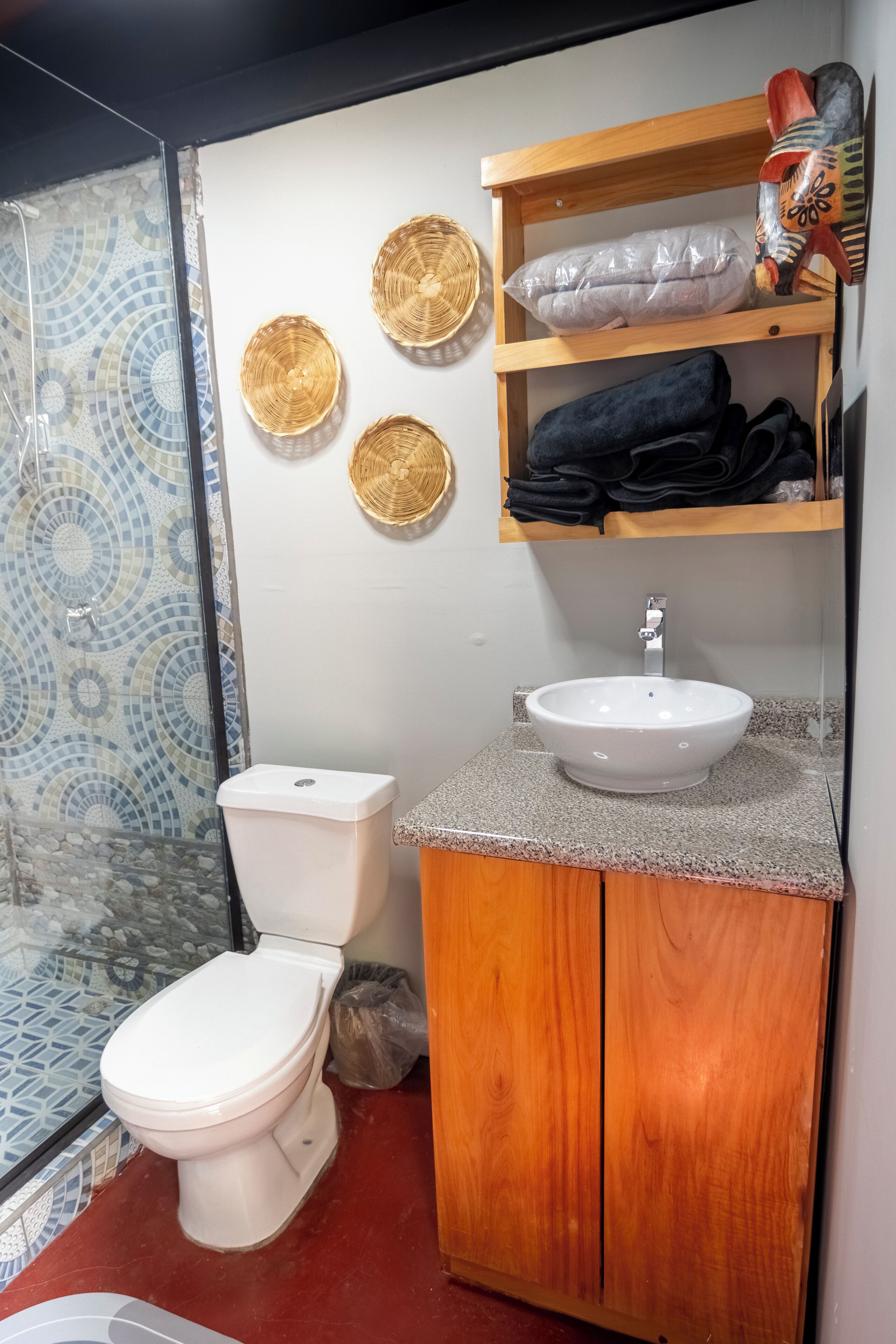 Un baño con inodoro, lavamanos y ducha. Hay cestas decorativas en la pared y un estante con toallas.
