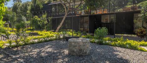 Un espacio exterior moderno con una jardinera de piedra, suelo de grava y un edificio con techo metálico.