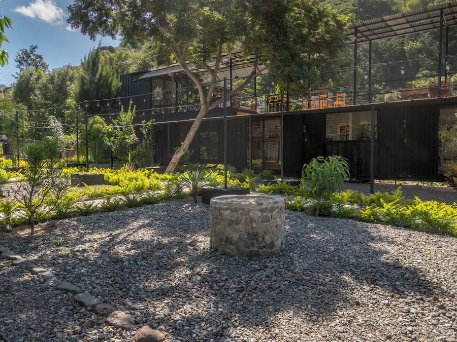A modern outdoor area with a stone planter, gravel ground, and a building with a metal roof.