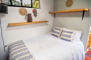 Un dormitorio con cama, almohadas, una mesita de noche y estantes en la pared.