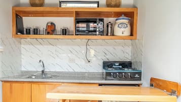Cocina compacta con encimera de madera, horno integrado y barra con taburetes.