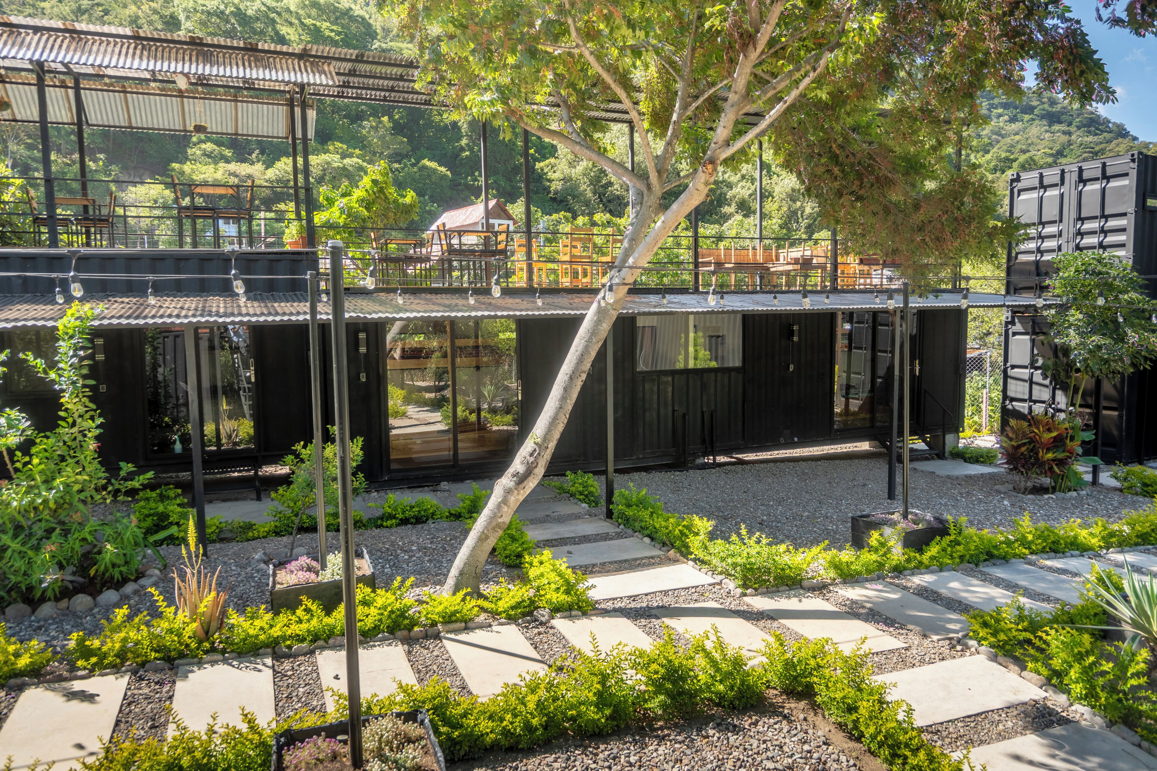 Un edificio moderno con jardín en la azotea, asientos exteriores y vistas a una ladera boscosa.