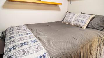 Een bed met gestreken beddengoed, een houten plank erboven en een wandplank.
