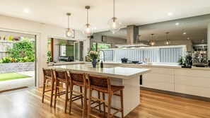 Una cocina moderna con una isla central, taburetes de bar, iluminación colgante y vistas al jardín exterior.