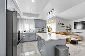 A modern kitchen with grey cabinets, a marble countertop, and a central island. - Spacious 7BR/5BA 8 Beds w/Hot Tub | Near & Airport (Las Vegas)