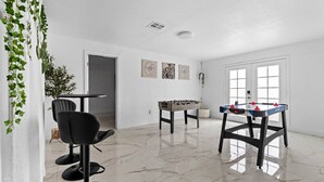 Una habitación amplia con una mesa de fútbol de mesa, una silla negra y una planta en maceta.