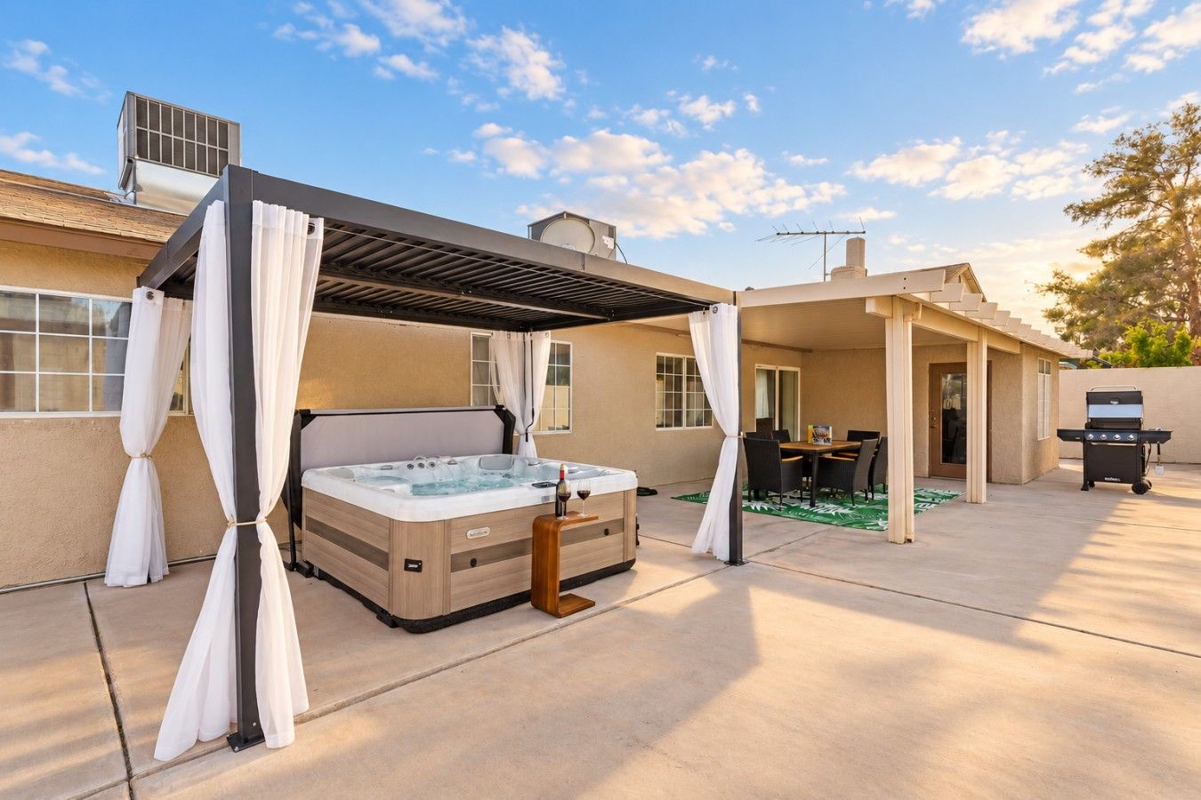A covered outdoor area with a hot tub, a grill, and a dining table.