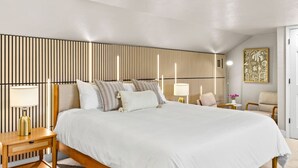 Ein Schlafzimmer mit einem großen Bett, Nachttischen, einem Sessel und einer Wand mit vertikalen Linien.